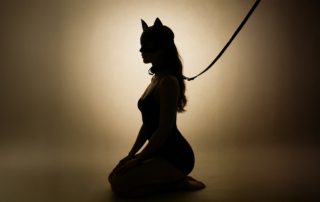 silhouette of a woman in a cat mask kneeling on a flor tied to a leash